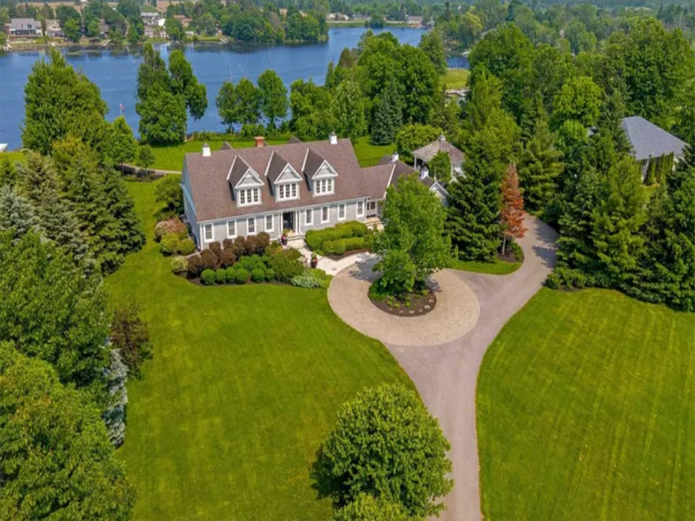 Front view of 6029 Rideau Valley Drive North, Ottawa — elegant single-family home with manicured lawn, mature trees, and a spacious driveway.